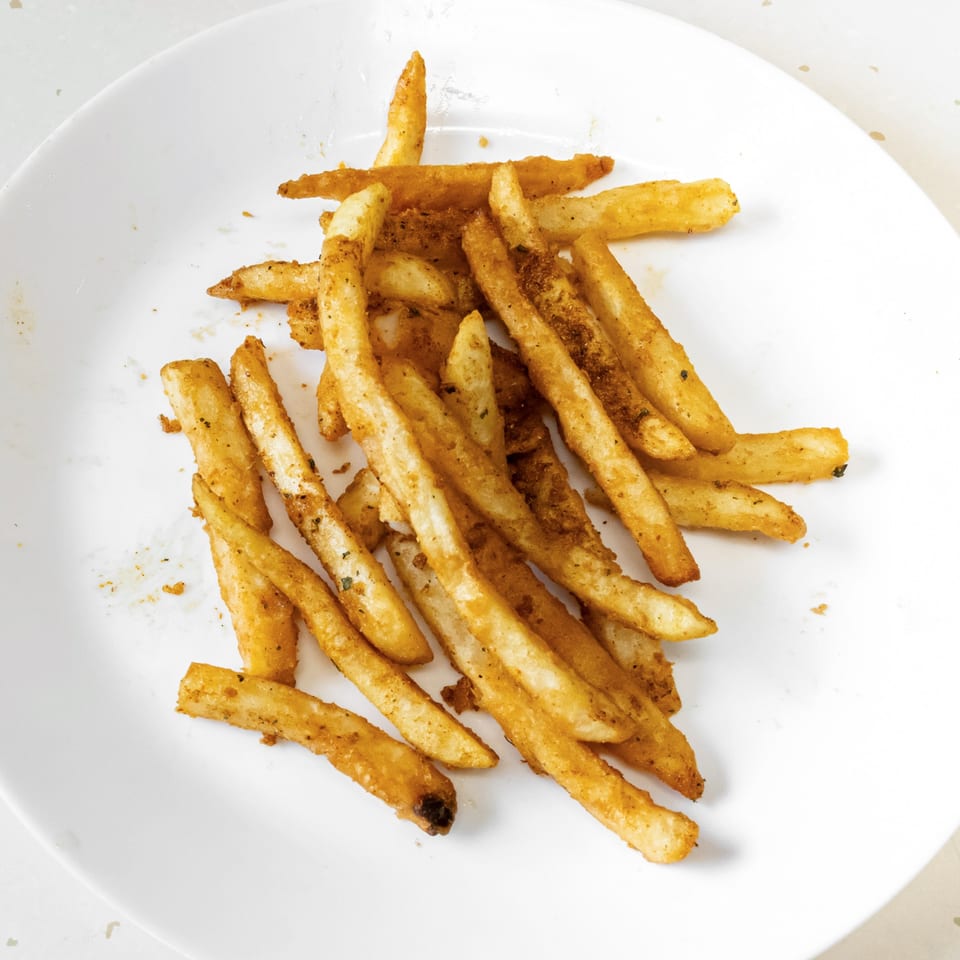 A white plate piled high with golden-brown, seasoned French fries from Fried Shack.