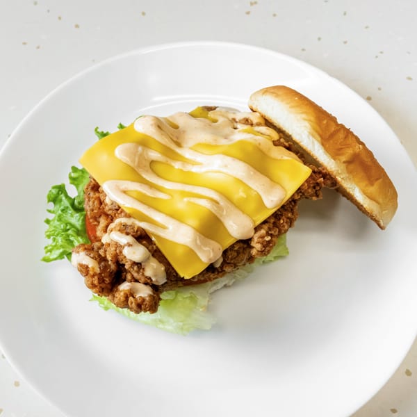 Fried Shack's fried chicken sandwich with melted cheese, sauce, lettuce, and tomato on a bun.