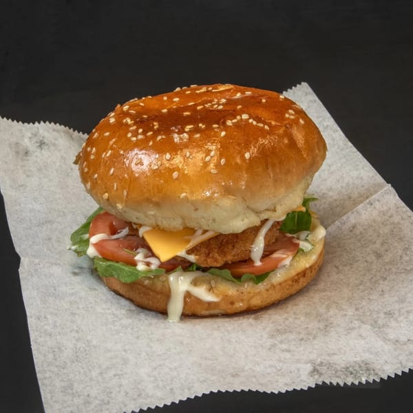 Fried Shack fried chicken sandwich with cheese, lettuce, tomato, and sauce on a sesame bun.