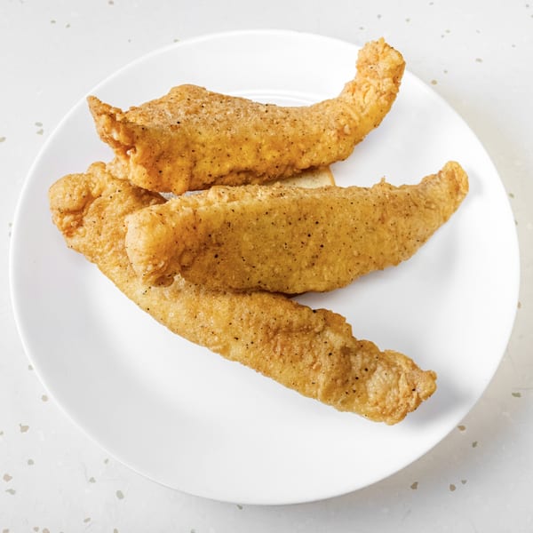 Three golden-brown fried chicken tenders, seasoned with pepper, arranged on a white plate.