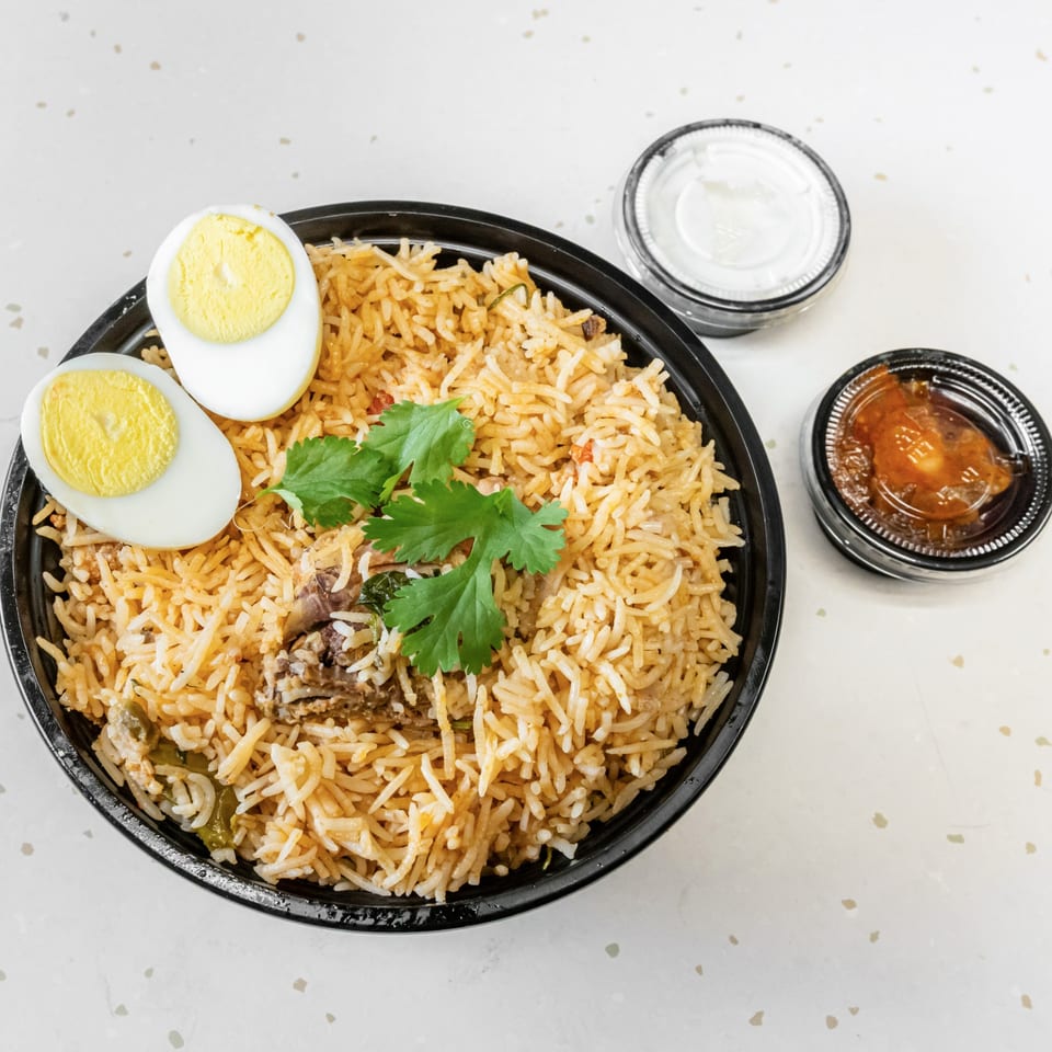 Fried Shack's chicken biryani with two hard-boiled egg halves, cilantro, and two sauce containers.